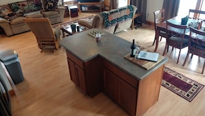 Amplia sala de estar con una isla central grande, comedor con sillas de madera y una zona de estar acogedora con cojines estampados.