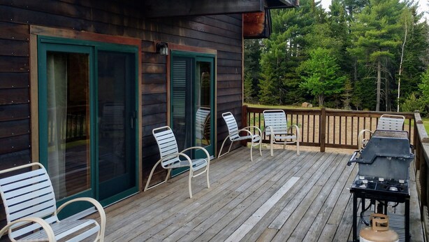 Una terraza de madera con mobiliario exterior y una parrilla.