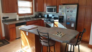 Una cocina con gabinetes de madera, un refrigerador de acero inoxidable, un microondas, una estufa y una zona de bar con sillas.