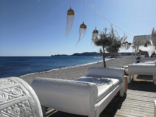 A beachside seating area with white benches and hanging lanterns, overlooking the sea.