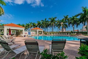 A swimming pool with lounge chairs, a covered seating area, and palm trees in the background. - Club Bahia Island Sunsets (St Petersburg)