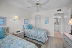 Ein Schlafzimmer mit zwei Betten, einem Nachttisch, einer Lampe und einem Deckenventilator.