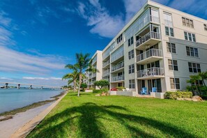 A multi-story hotel with balconies, a grassy lawn, and a view of a bridge over water. - Club Bahia Island Sunsets (St Petersburg)