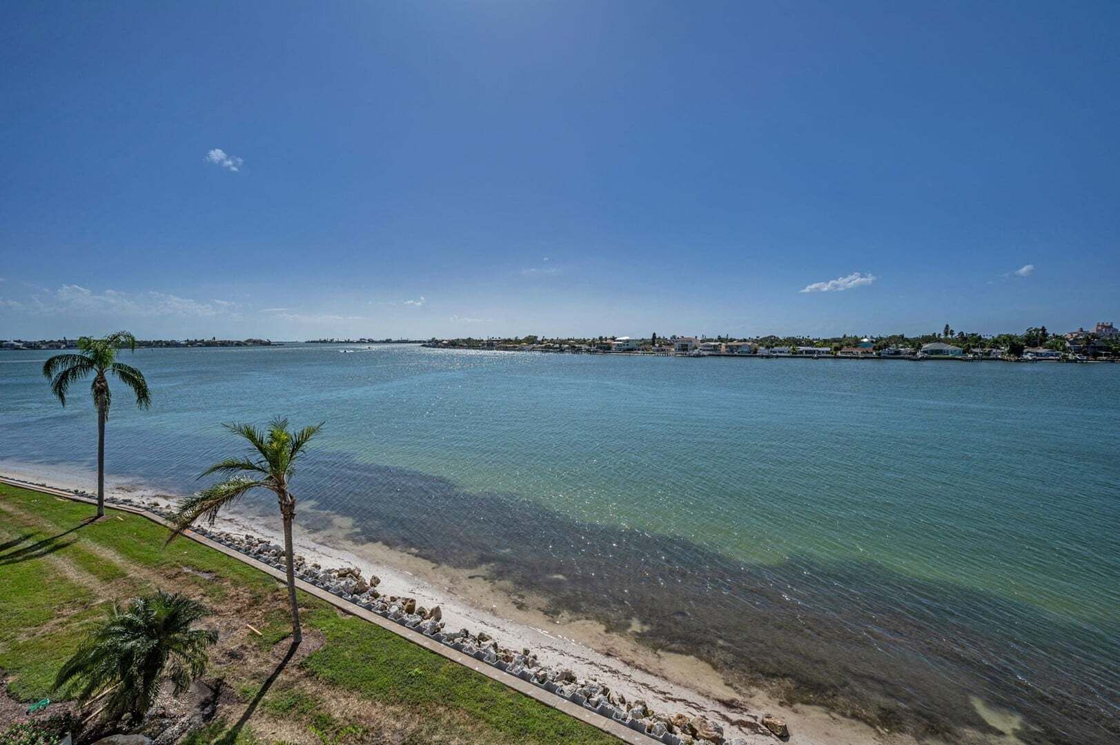 Une vue sur la côte, avec une eau claire, une plage de sable et une ligne de rivage lointaine où se trouvent des bâtiments.