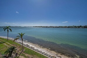 A coastal view with clear water, a sandy beach, and a distant shoreline with buildings.