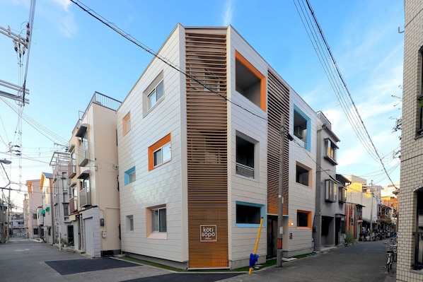 Un edificio moderno de varios pisos con techo inclinado, ventanas amplias y una entrada visible.