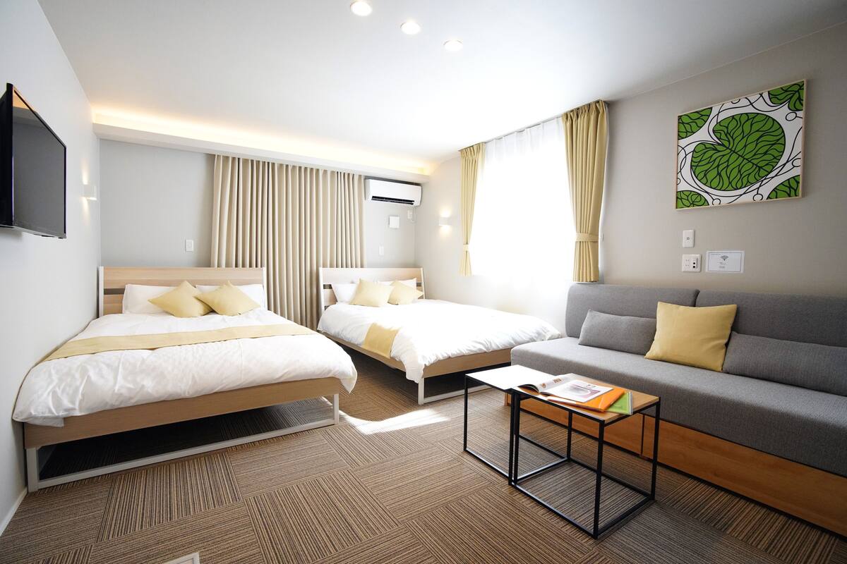 Habitación de hotel con dos camas individuales, un sofá, una mesa de centro y un televisor de pantalla plana.
