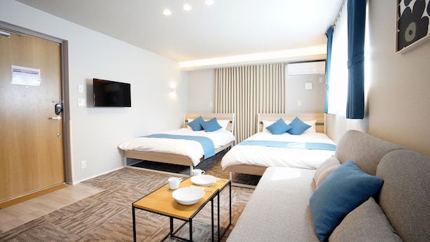 A hotel room with two beds, a sofa, a small table, and a flat-screen TV. - Koti Sopo Universal Bay 1 by Liaison (Osaka)