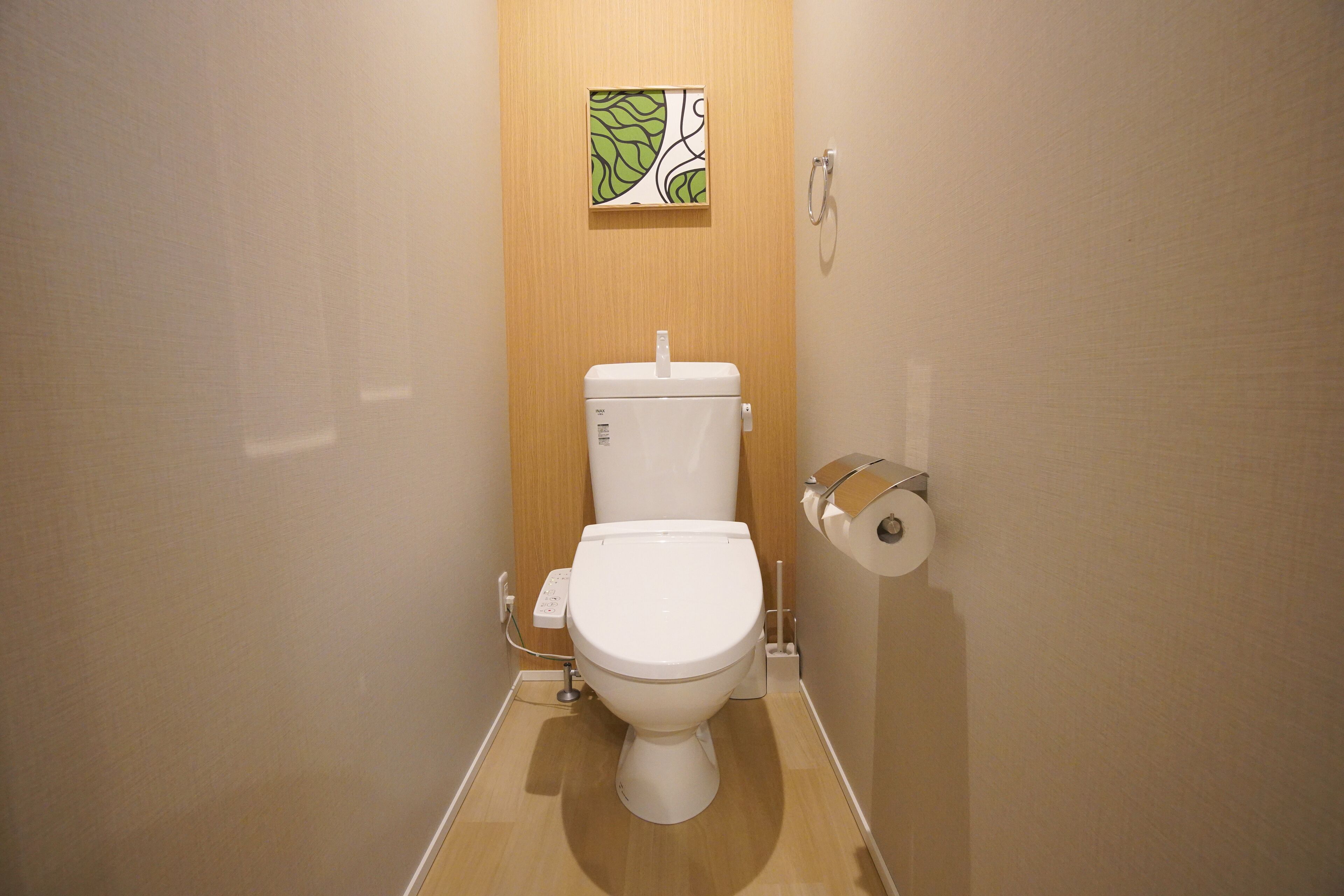A small, modern bathroom with a toilet, a toilet paper holder, and a wooden panel with a leaf pattern.