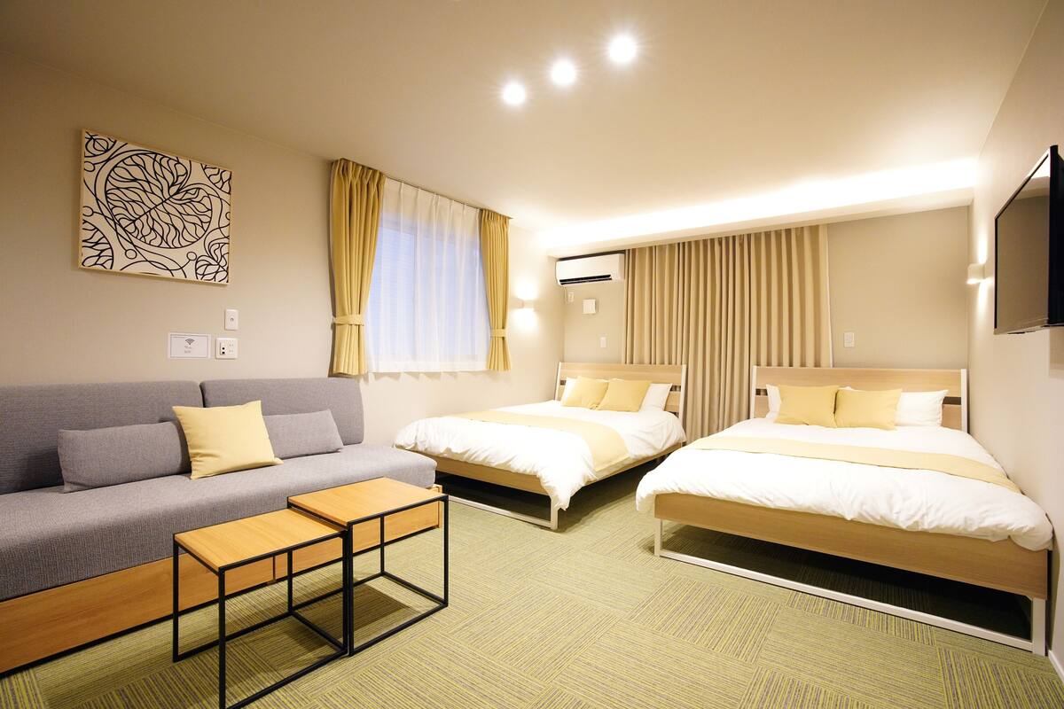 Una habitación de hotel con dos camas, un sofá, una mesita y un televisor montado en la pared.