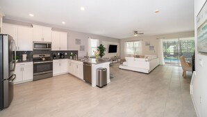 A spacious kitchen with modern appliances, a dining area with a white sofa, and large windows offering a view of the outdoors. - JMT2705 Storey Lake Home 7Beds 5Baths Private Pool with Spa and Free Waterpark (Kissimmee)