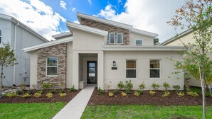 A modern two-story house with a stone facade, a front entrance, and a well-maintained lawn. - JMT2705 Storey Lake Home 7Beds 5Baths Private Pool with Spa and Free Waterpark (Kissimmee)