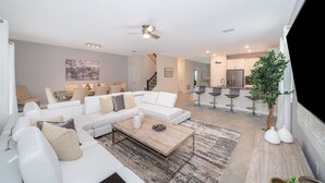 A modern living room with a white sofa set, a coffee table, and a dining area with chairs. - JMT2705 Storey Lake Home 7Beds 5Baths Private Pool with Spa and Free Waterpark (Kissimmee)
