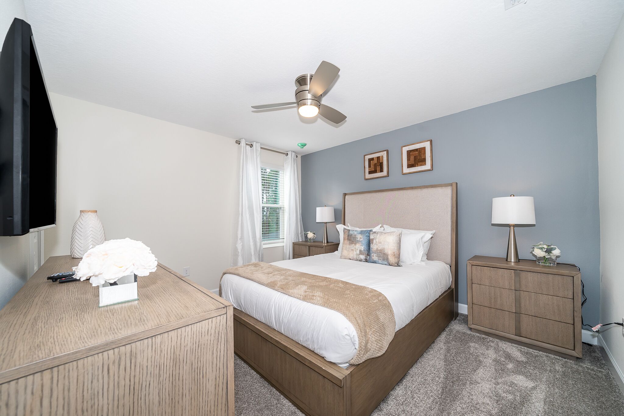 A bedroom with a bed, bedside tables, a ceiling fan, and a TV.