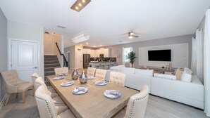 A modern living room with a dining area, white furniture, a flat-screen TV, and a staircase leading to an upper level. - JMT2705 Storey Lake Home 7Beds 5Baths Private Pool with Spa and Free Waterpark (Kissimmee)