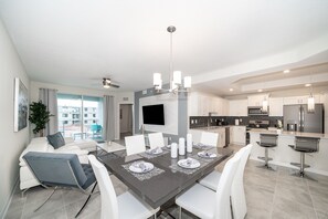 A modern kitchen with stainless steel appliances, a dining area with a dark table and white chairs, and a large window offering a view of the city.