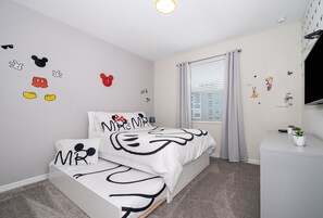 A bedroom with a bed, a nightstand, and Mickey Mouse-themed decor.