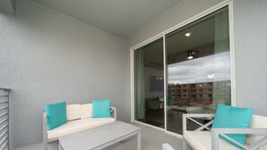 Ein Balkon mit einer weißen Couch und Sesseln, einem kleinen Tisch und einer Glastür zu einem Innenbereich.