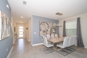 A dining area with a table set for four, a chandelier, and a large abstract painting on the wall. - (WE2738) Storey Lake Home 5/5, Private Pool & Free Waterpark (Kissimmee)