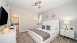 A bedroom with a bed, a nightstand, a TV, a ceiling fan, and a door leading to a bathroom. - (WE2738) Storey Lake Home 5/5, Private Pool & Free Waterpark (Kissimmee)