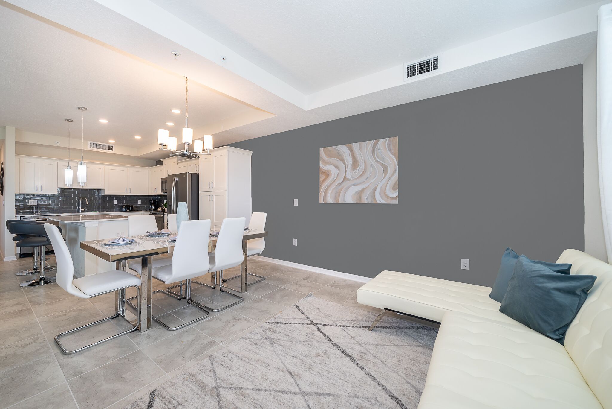 A modern kitchen with white cabinets, a dining area with a white table and chairs, and a gray accent wall.