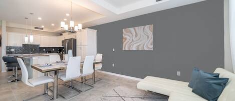 A modern kitchen with white cabinets, a dining area with a white table and chairs, and a gray accent wall.