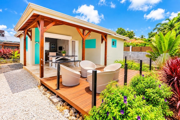 A covered outdoor seating area with a table and chairs, surrounded by a wooden deck and garden.