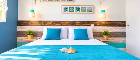 Un lit avec une literie bleue, deux oreillers, un coquillage décoratif et des œuvres d’art murales avec des motifs inspirés de la nature.