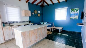 A kitchen with a central island, a dining area with a bench, and a wall with decorative plates. - --- AIGUE-MARINE --- (Sainte-Anne)