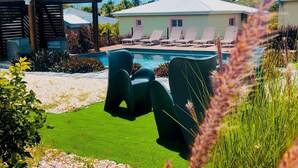 A pool area with lounge chairs, a covered seating area, and a building with a white roof. - --- AIGUE-MARINE --- (Sainte-Anne)