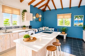 A modern kitchen with a central island, a dining area with bar stools, and a living space with a sofa.