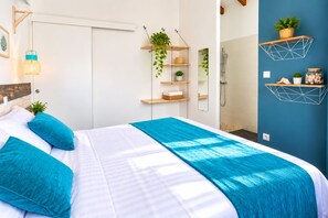 A bedroom with a bed, a nightstand, a wall-mounted shelf with plants, a hanging light, and a bathroom with a shower.