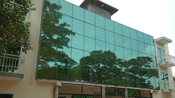 Een modern gebouw met grote glasramen die bomen reflecteren, een plat dak en een balkon op de bovenste verdieping.
