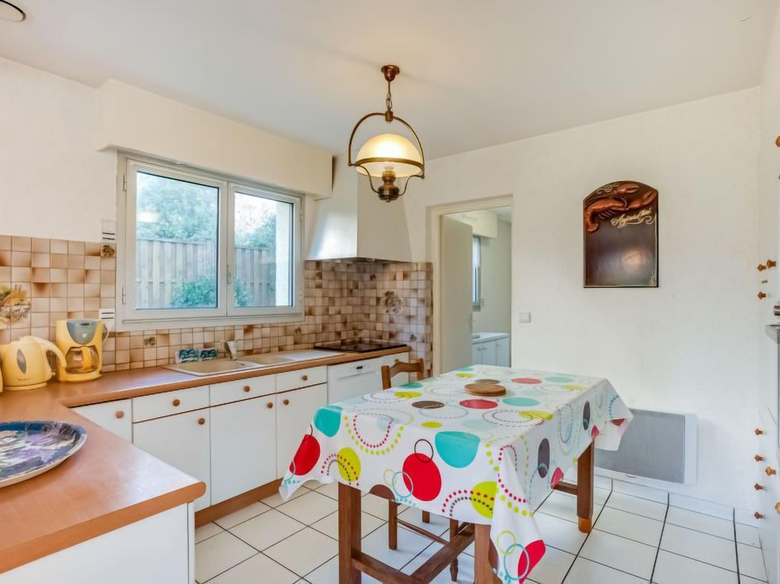 Una cocina con armarios blancos, un salpicadero de azulejos, una ventana y una mesa con mantel colorido.