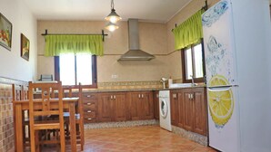 A kitchen with wooden cabinets, a washing machine, a refrigerator with a lemon design, and a dining area with chairs. - Chalet Dehesa Villa with private pool (CONIL DE LA FRONTERA)