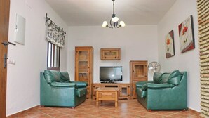 A living room with two green leather sofas, a wooden TV stand, a chandelier, and a fan. - Chalet Dehesa Villa with private pool (CONIL DE LA FRONTERA)