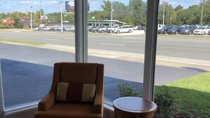 A room with a large window, a brown armchair, and a small wooden table. - Ocala Cove Motel (Ocala)
