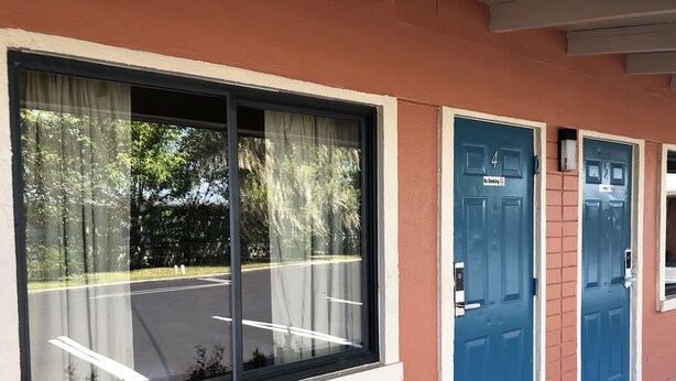 A building with large windows, blue doors, and a parking lot visible through the windows. - Ocala Cove Motel (Ocala)
