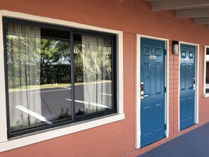 A building with large windows, blue doors, and a parking lot visible through the windows. - Ocala Cove Motel (Ocala)