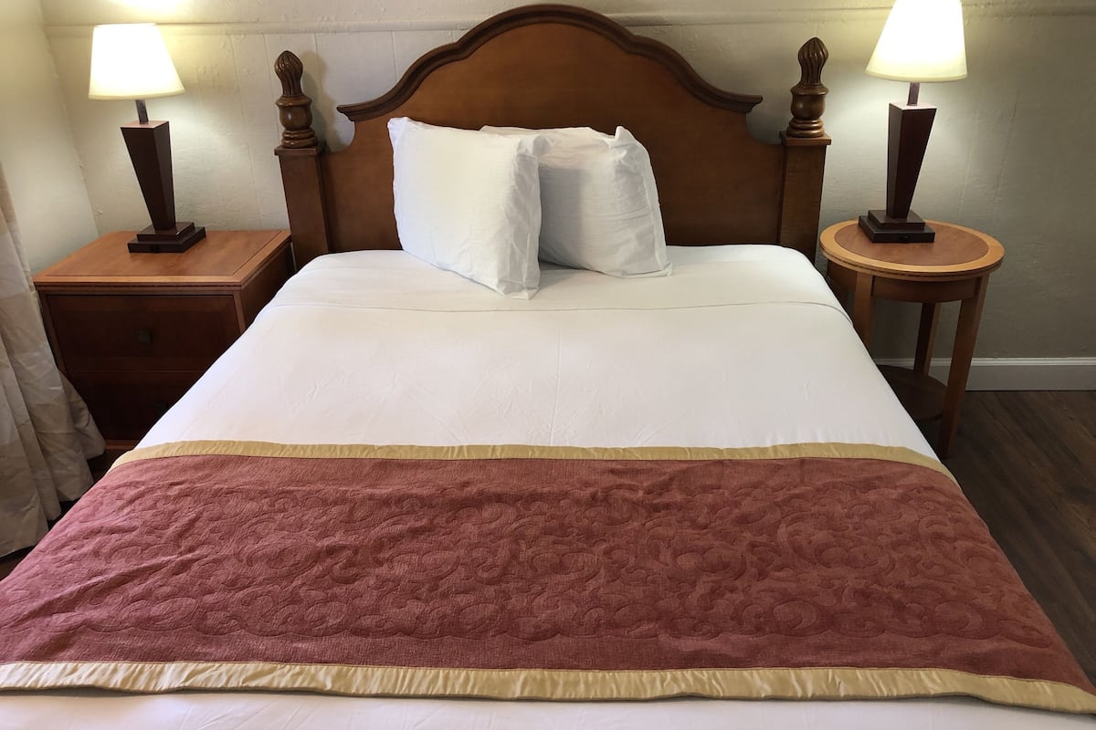 A neatly made bed with a white and pink blanket, two bedside lamps, and a wooden headboard.