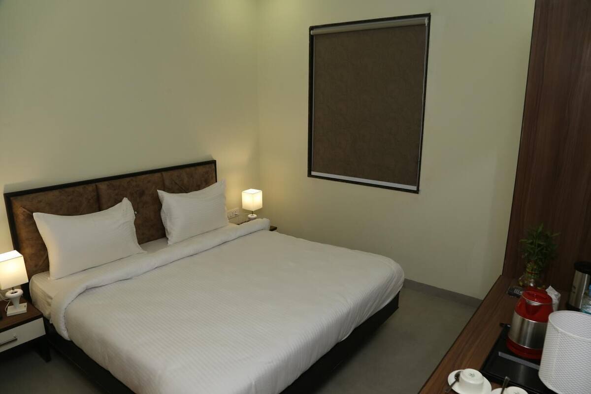 Hotelkamer met een bed, nachtlampjes, een nachtkastje, een houten hoofdeinde, een wandgemonteerde televisie en een bureau met een koffiezetapparaat en een plant.