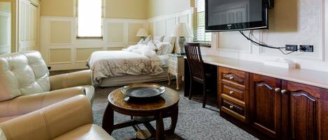 Una habitación de hotel con cama, sofá, mesa de comedor y televisor montado en la pared.