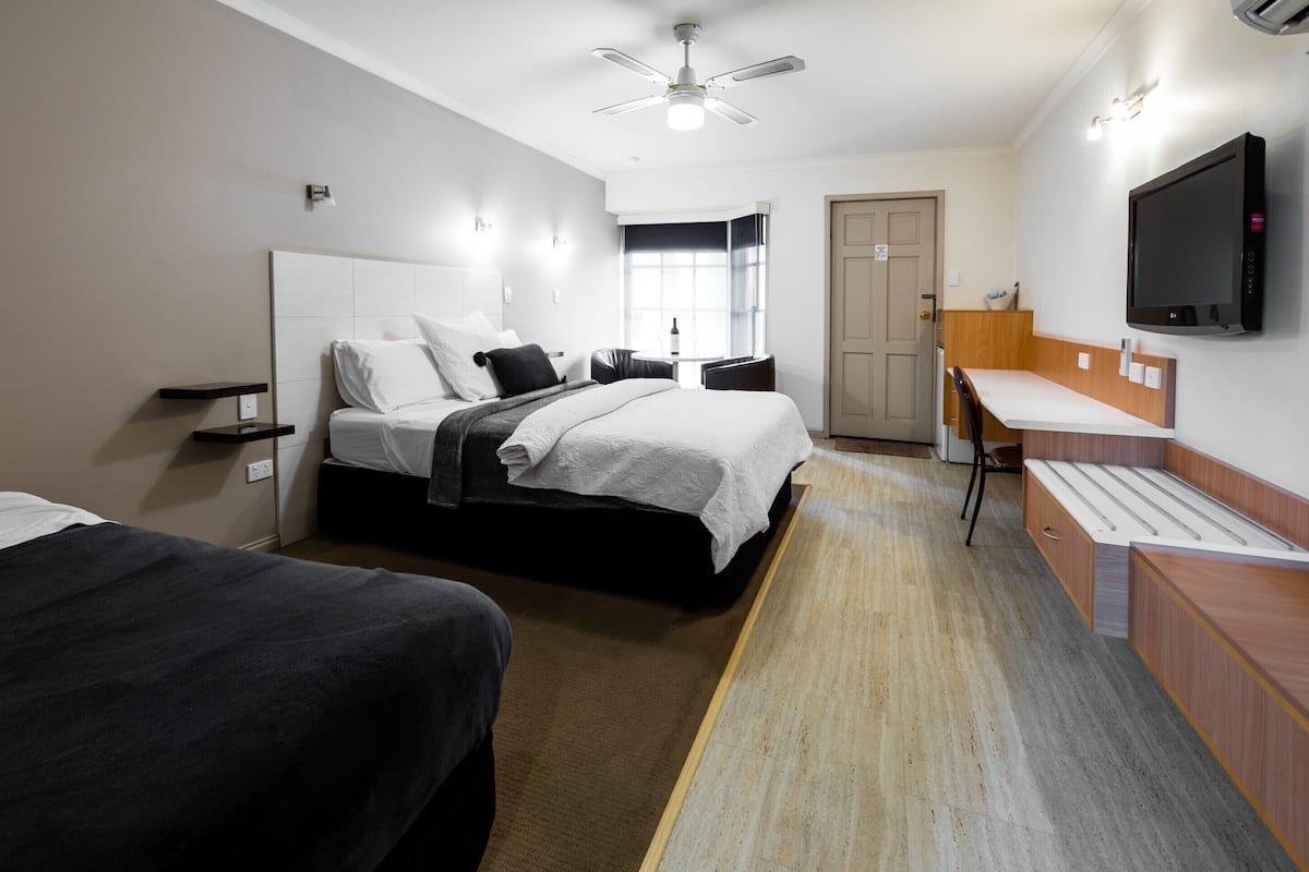 A hotel room with a bed, bedside tables, a desk, a chair, a TV, and a ceiling fan.