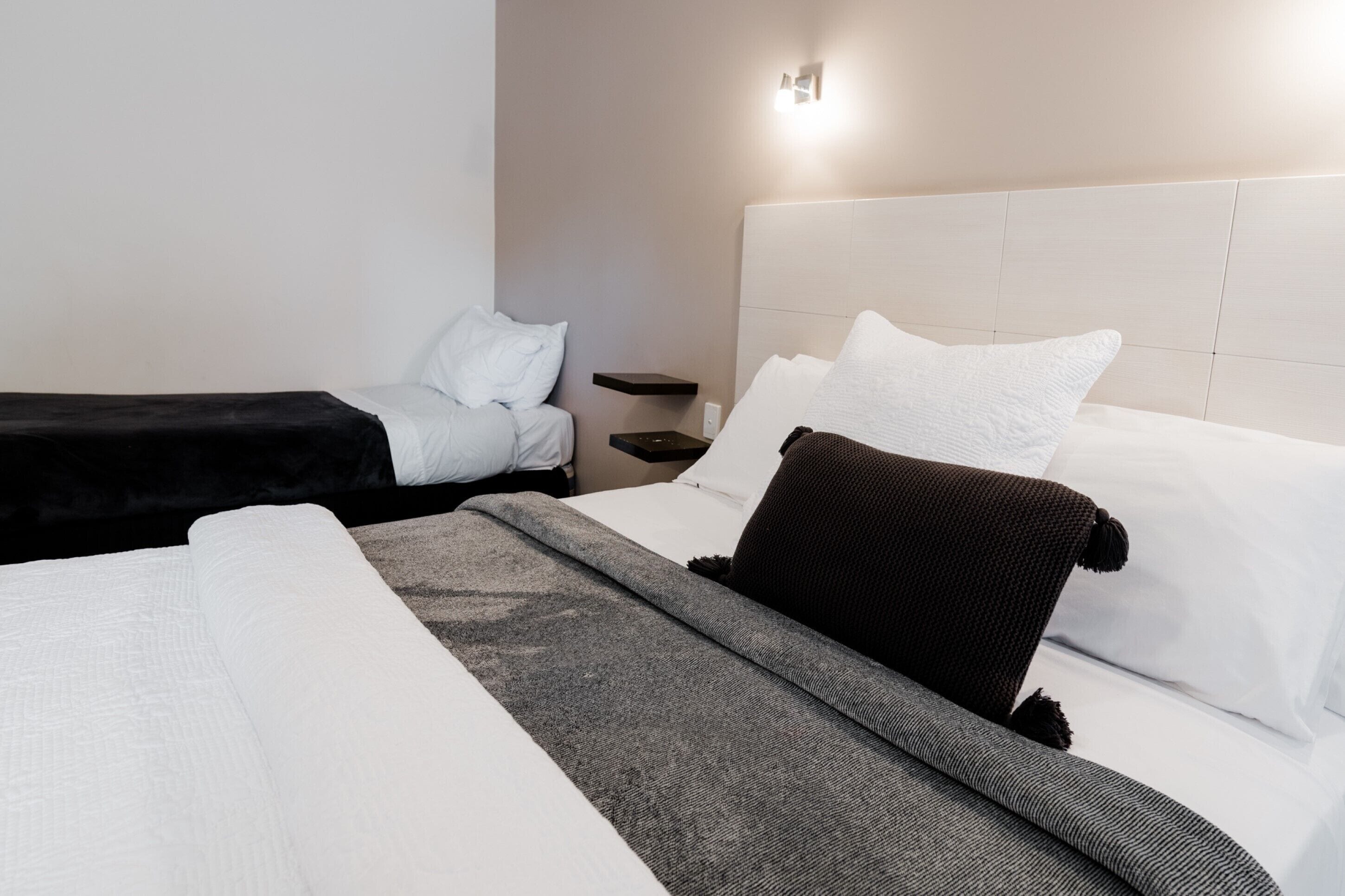 A hotel room with two beds, a nightstand, and a wall-mounted light fixture.