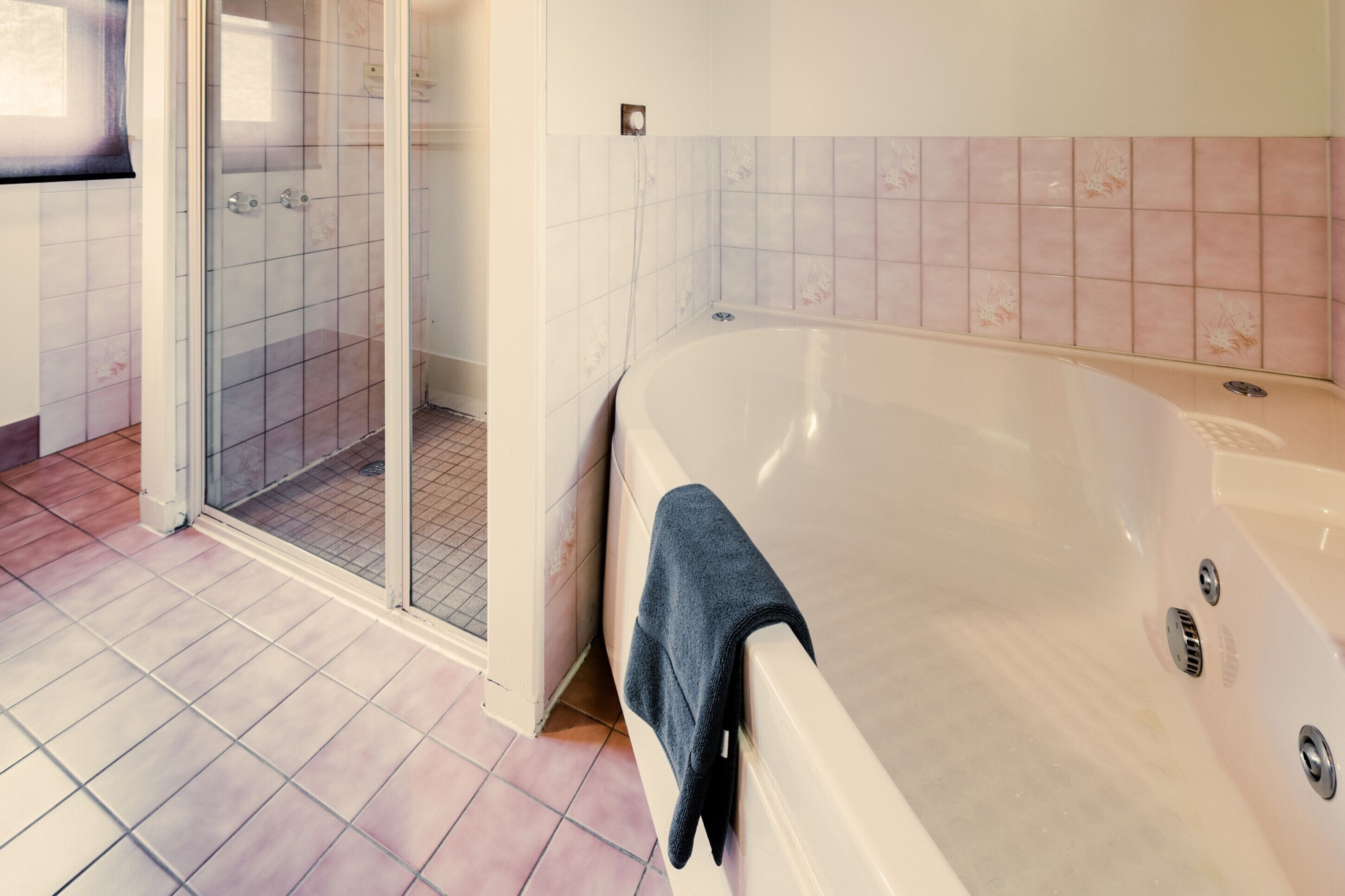 Un baño con bañera, zona de ducha y paredes de azulejos.