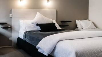 A modern bedroom with a bed, white pillows, a black pillow, and a grey blanket. There are two wall-mounted light fixtures above the bed.