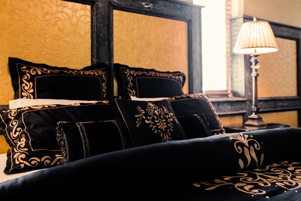 A bed with black and gold pillows, a lamp, and a patterned wall.