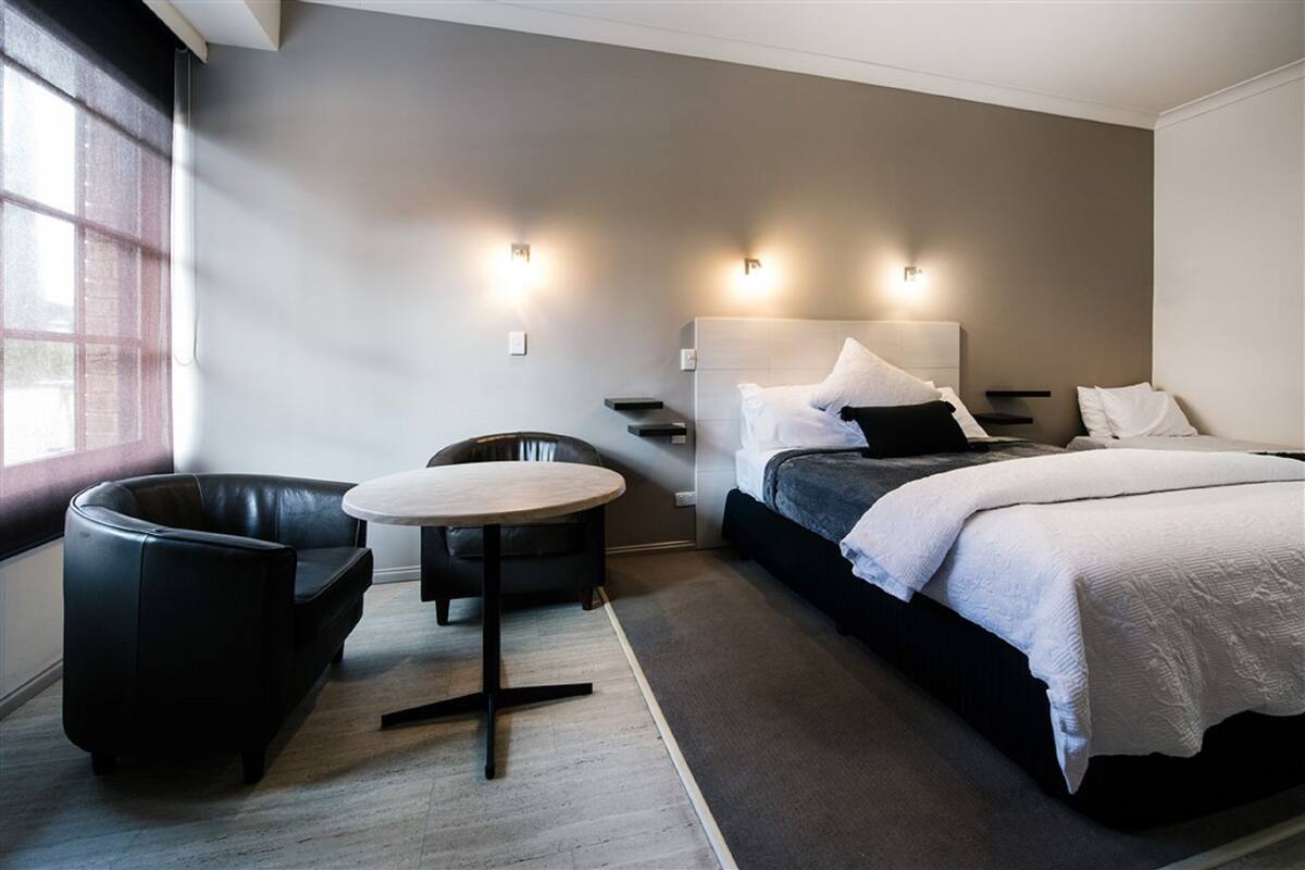 A modern hotel room with a bed, a round table, a leather chair, and a window.