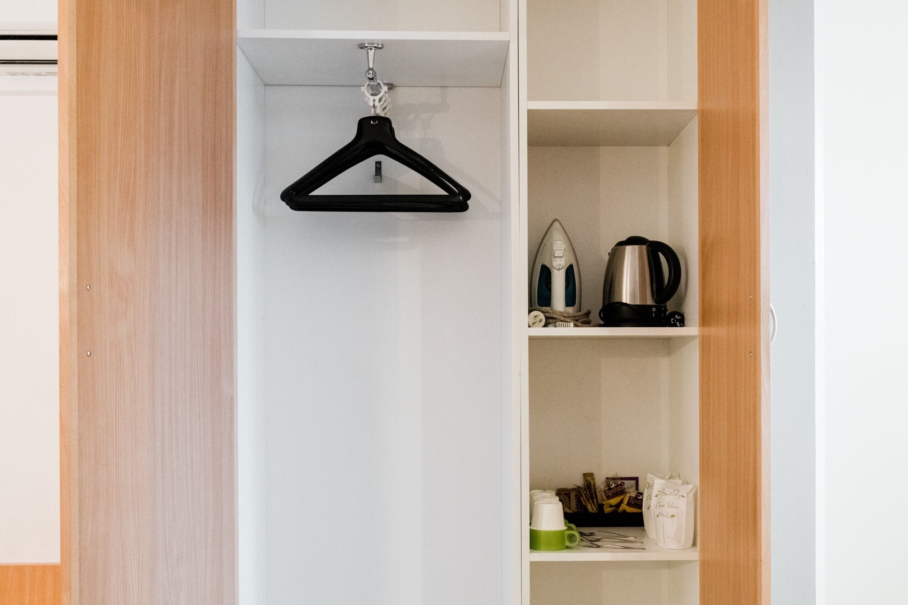 A white closet with a black hanger on a hook. Inside, there are shelves with a kettle, a coffee maker, and bags.