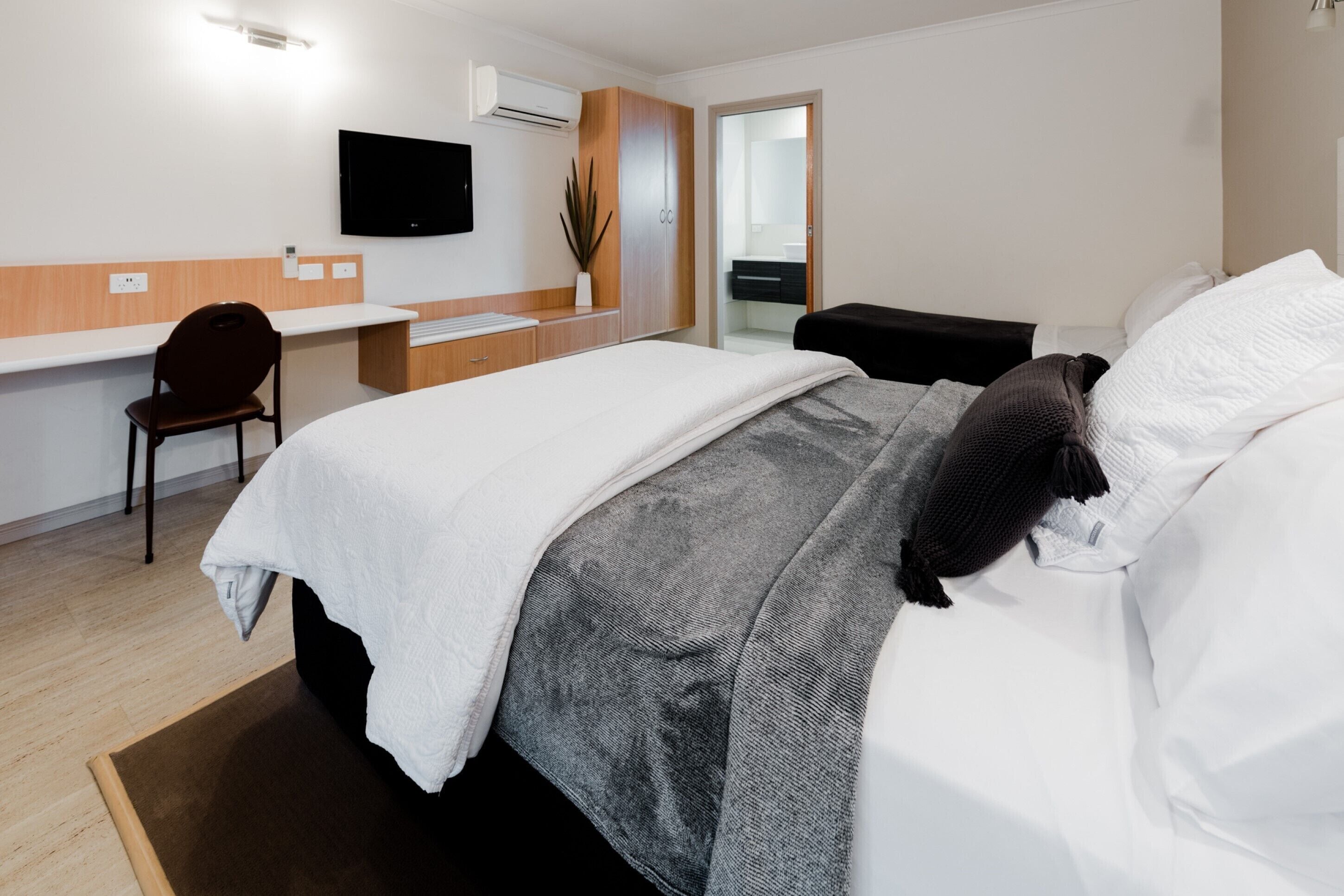 Ein Hotelzimmer mit Bett, Schreibtisch, Stuhl, Fernseher und einem durchgegangenen Tür sichtbaren Badezimmer.
